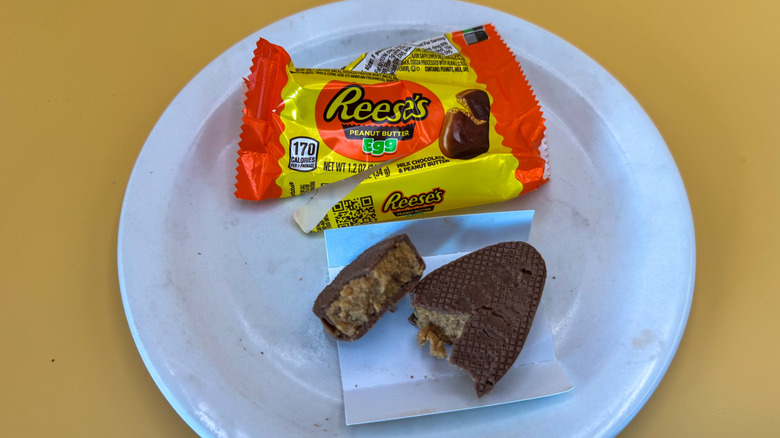 Reese's egg broken in half on a white plate next to open wrapper on a yellow background