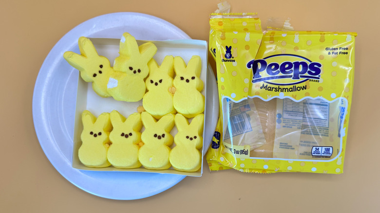 Eight yellow bunny-shaped Peeps candy in cardboard tray on plate next to candy wrapper on a yellow background