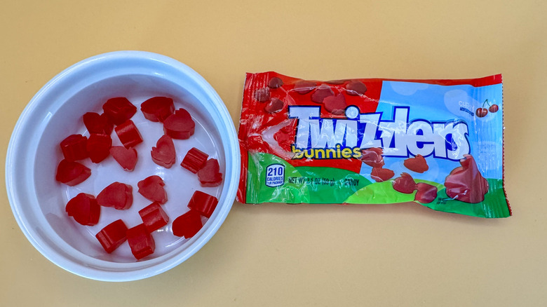 Twizzlers bunnies scattered in the bottom of a white ramekin next to a package of the candy on a yellow background