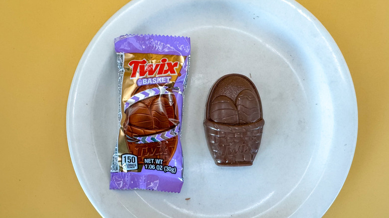 Twix Basket candy wrapper next to chocolate shaped like a filled Easter basket on a white plate and a yellow background