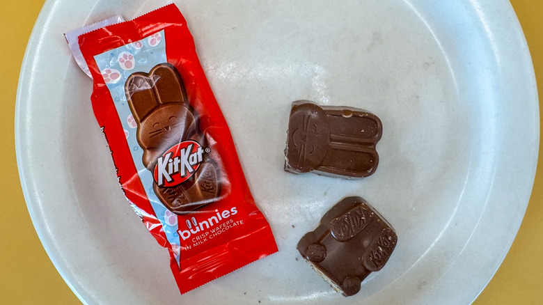 Kit Kat bunnies packaging on a white plate next to one chocolate bunny candy broken in half with a yellow background