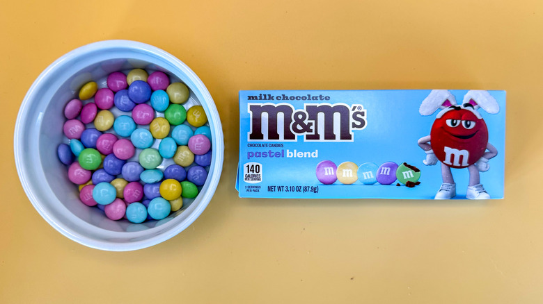 Milk chocolate pastel blend candies in a ramekin next to box on a yellow background