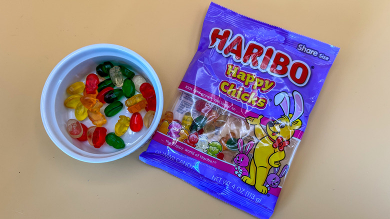 Multicolored Harbio Happy Chicks candy in a white ramekin next to packaging on a yellow background