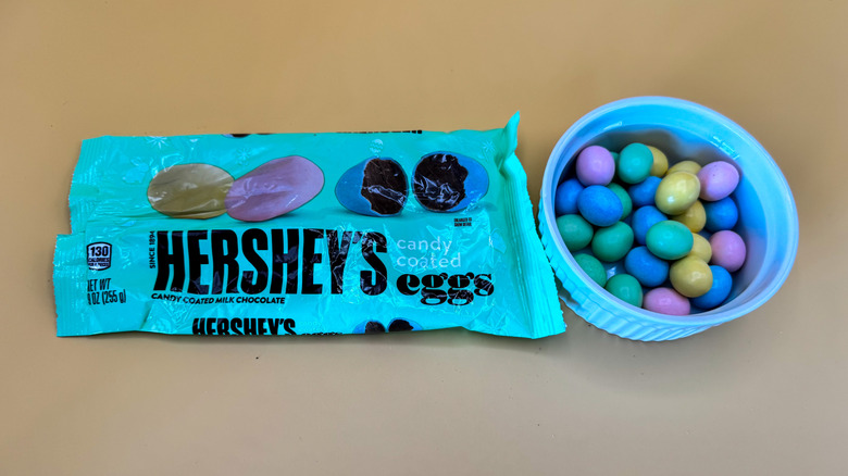 Hershey's multicolored eggs in blue ramekin next to packaging on a pale yellow background