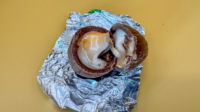Gooey milk chocolate egg split in half on opened foil wrapper sitting on a yellow background