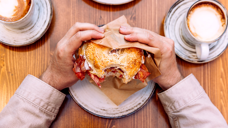 hands holding toasted bagel breakfast sandwich