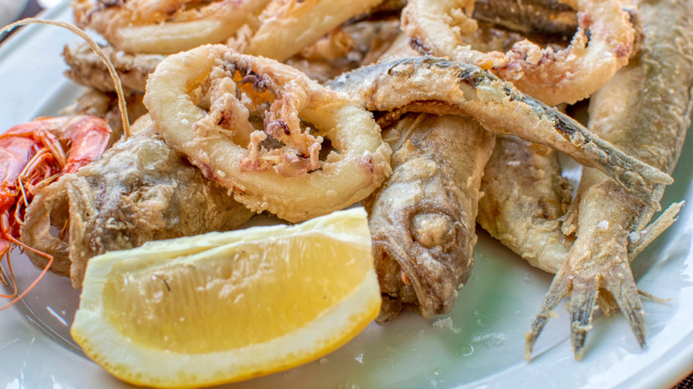 A plate of small fried fish, prawns, and calamari with a lemon wedge