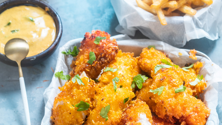 Fried breaded fish and a bowl of sauce on a blue tablecloth