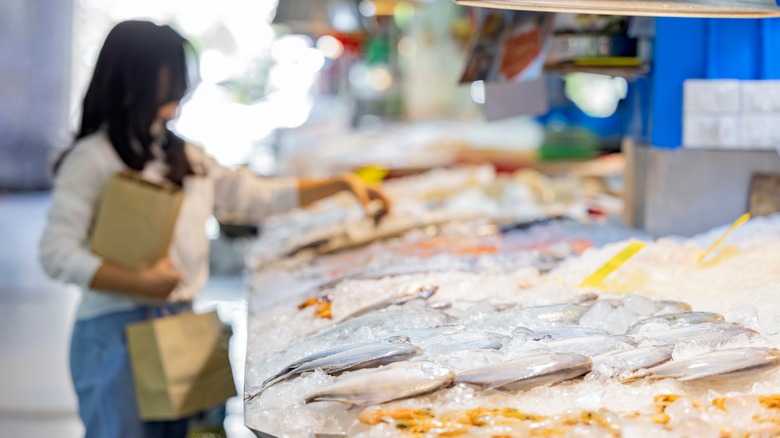 A person choosing seafood on ice from a counter in a store