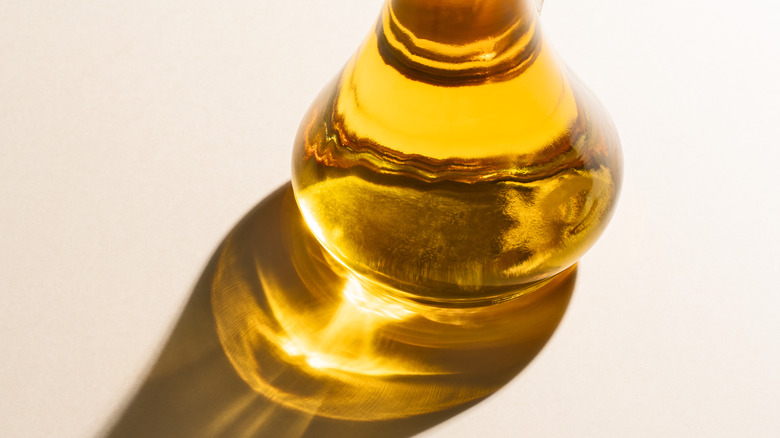 A glass bottle of oil with sunlight shining through it on a white surface