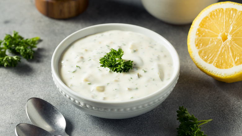 Tartar sauce in white bowl with a sprig of parsley on top and a halved lemon in the background