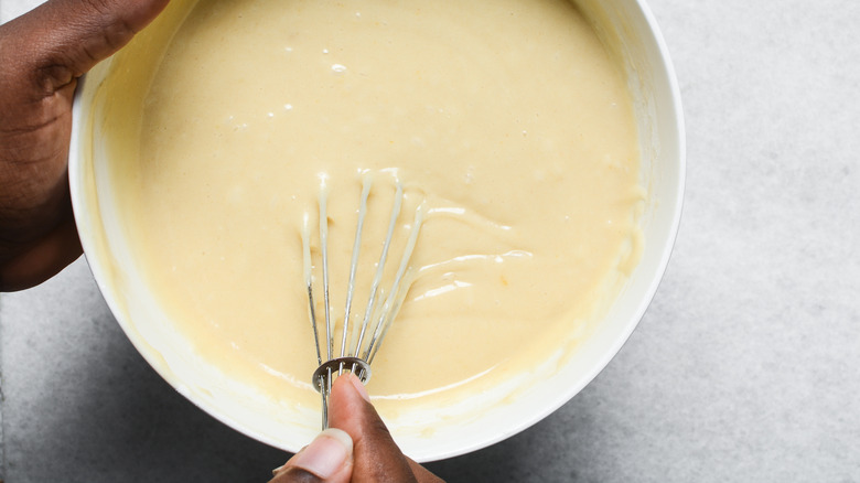 A person holding a whisk in a bowl of batter