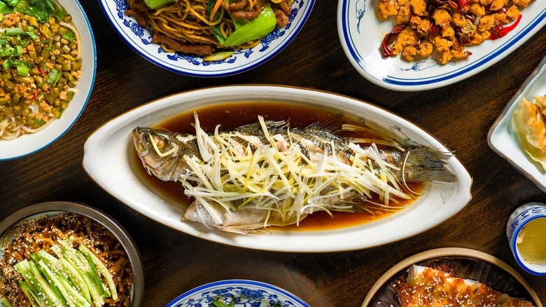 A fish sits in a dark sauce surrounded by other dishes such as fried chicken and noodles