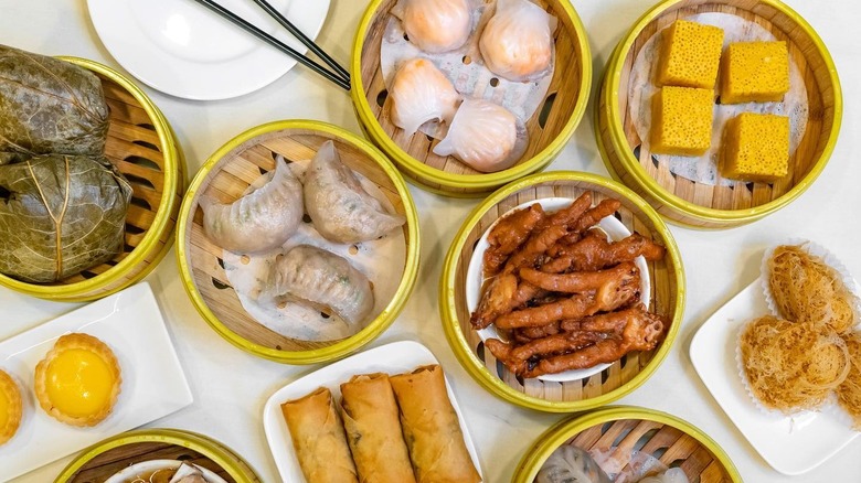 Several dim sum steam baskets with dumplings, chicken feet, and other items arranged on a white table