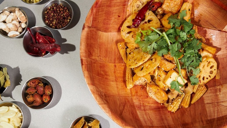 A wooden bowl with lotus root and several accompanying spices on a grey background