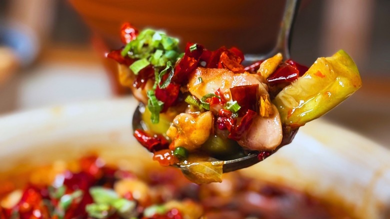 A spoonful of red chilis and chicken hovers over a dish