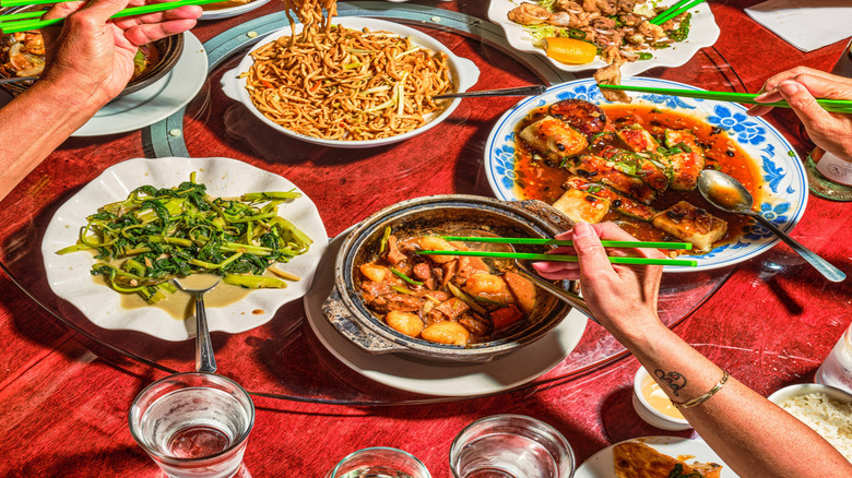 Several hands holding green chopsticks reach for bites from a variety of dishes