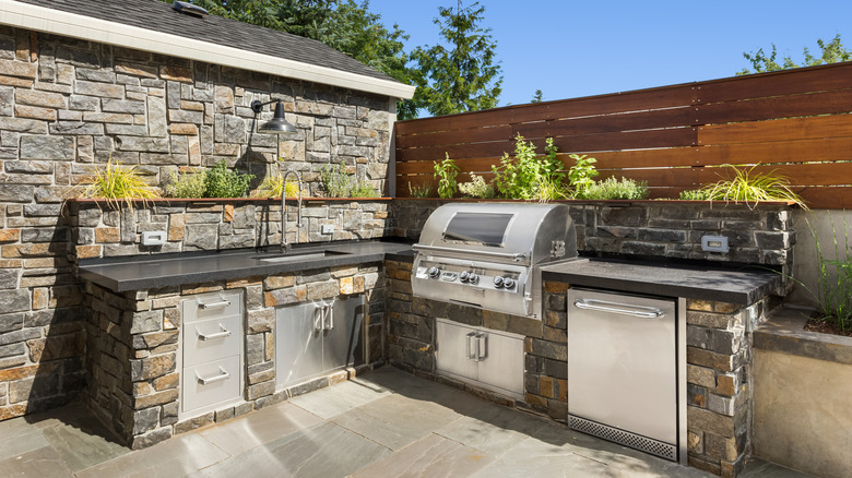 Corner outdoor kitchen with a sink, grill, dishwasher, and prep areas