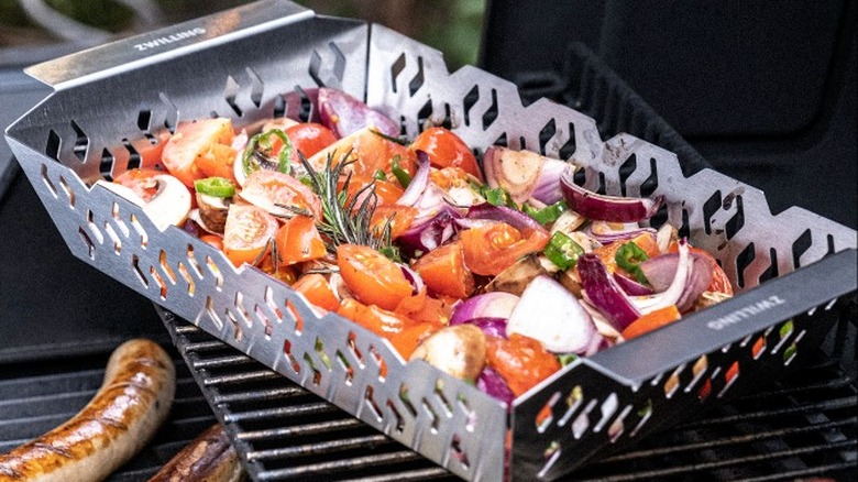 Grill basket with veggies in it, alongside sausage