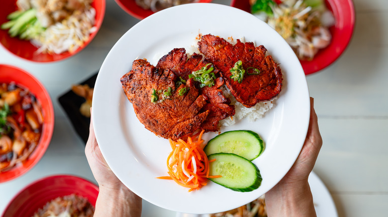 A person holding a plate of Cambodian grilled pork and rice