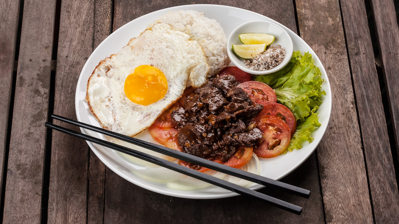 A plate of beef lok lac with a fried egg, rice, and vegetables