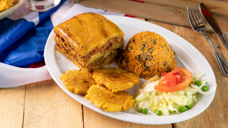 Plate of pastelón, fried plantains, and arroz con gandules