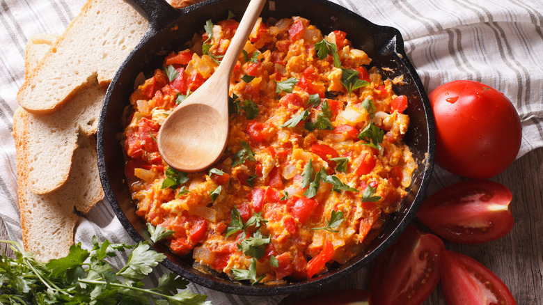 A skillet of Turkish menemen with tomatoes and bread on the side