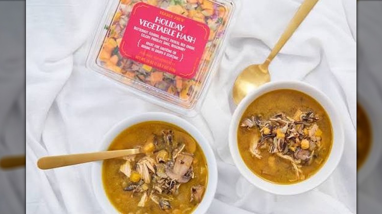 Plastic clamshell container of Trader Joe's Holiday Vegetable Hash next to white bowls filled with soup