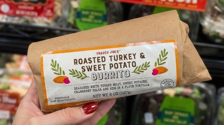 Person's hand holding up a Trader Joe's Roasted Turkey & Sweet Potato Burrito wrapped in brown paper