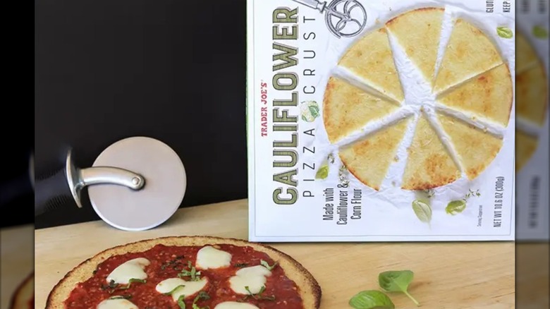 Trader Joe's cauliflower pizza crust next to pizza and pizza cutter
