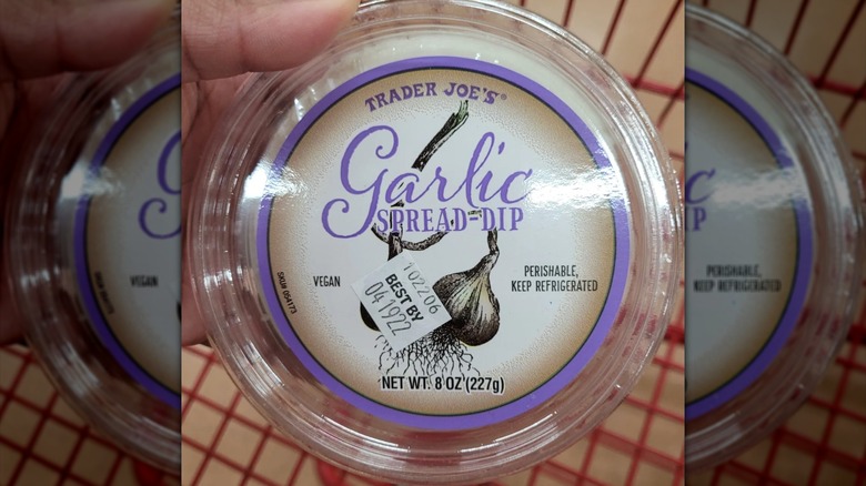 Woman holding container of Trader Joe's garlic spread in stores.