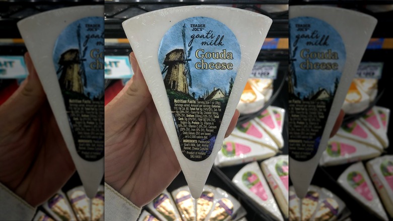 Shopper holding wedge of Trader Joe's goats milk gouda-style cheese in stores.