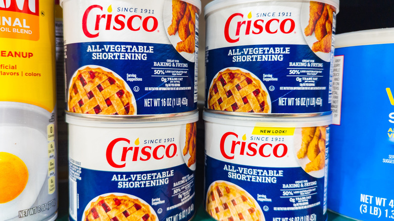 Four Crisco All-Vegetable Shortening cans displayed on a shelf at a supermarket.