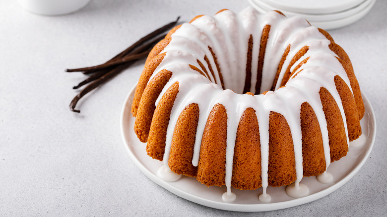 Bundt cake with white icing on plate beside vanilla beans