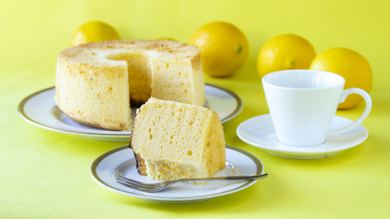 Chiffon cake with slice on plate beside a coffee mug and lemons in background