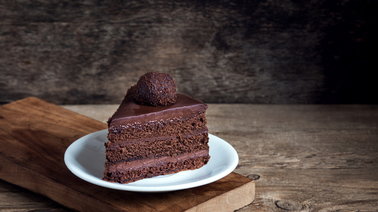 Chocolate cake slice on white plate on wooden serving board