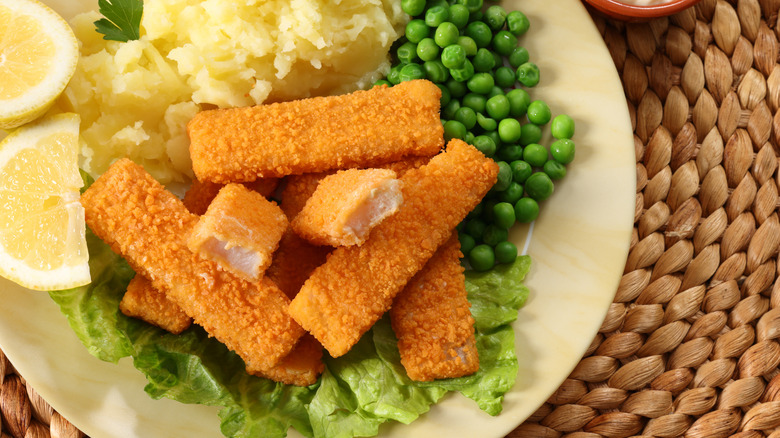 A plate of fish fingers on a plate with peas and mashed potatoes