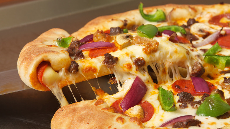 a stuffed crust pizza with one slice being lifted, showing a cheese pull