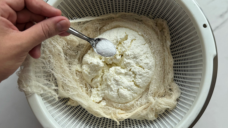 small spoon of salt held over strained curds