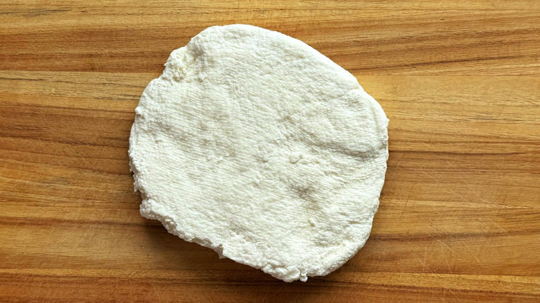 pressed disk of paneer on wooden cutting board