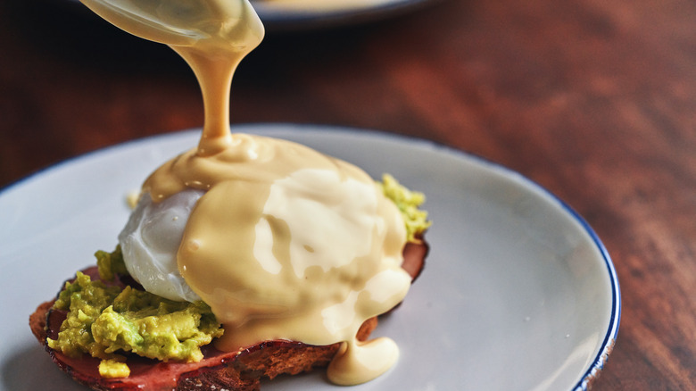 a spoon pouring hollandaise sauce over a piece of toast