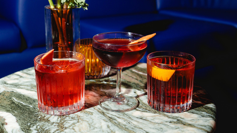 A Negroni in a coupe glass between two Negronis in rocks glasses