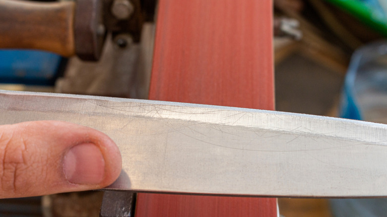 sharpening polishing kitchen knife blade on the grinder sander