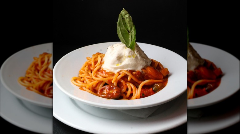 White bowl of spaghetti with heirloom tomato sauce topped with burrata cheese and basil