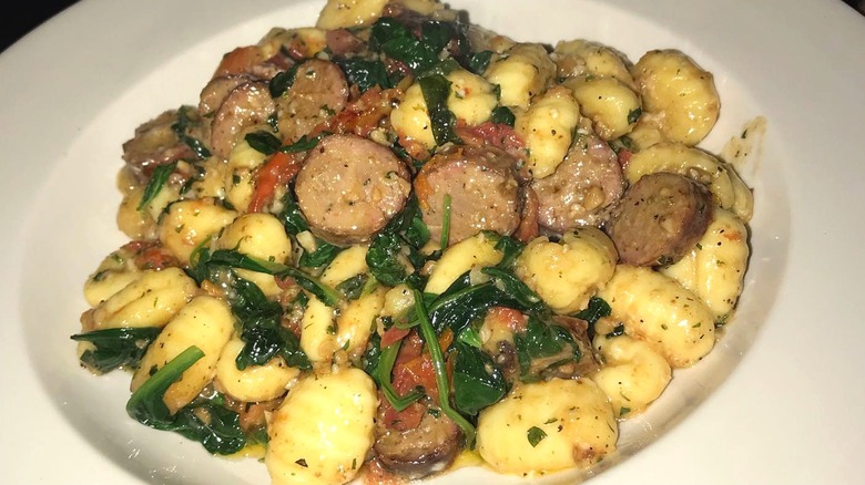 White bowl of gnocchi with sausage and spinach