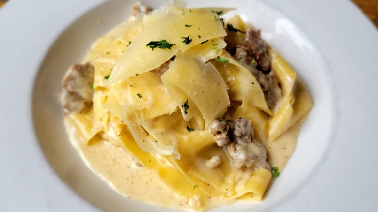 White bowl of homemade pasta with freshly shaved parmesan cheese on top