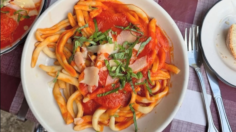 White bowl of pasta with tomato sauce, shaved parmesan cheese, and fresh basil