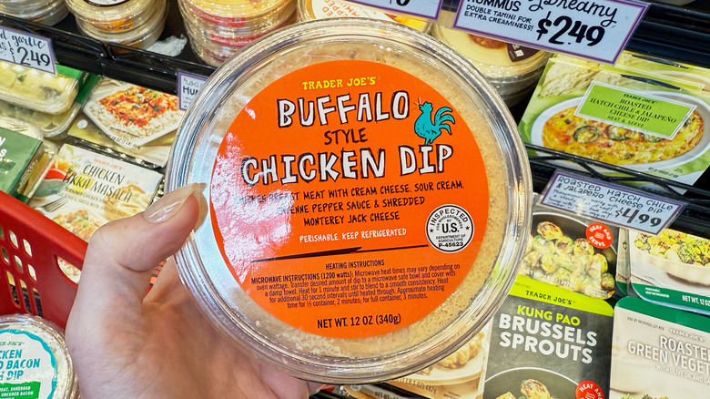 A hand holding a container of Trader Joe's buffalo chicken dip