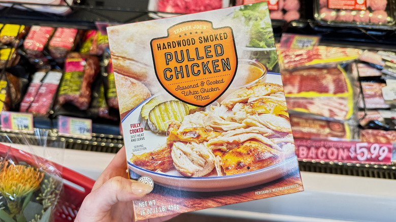 A hand holding a box of Trader Joe's Hardwood Smoked pulled chicken