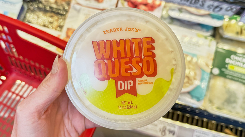 A hand holding a container of Trader Joe's white queso dip